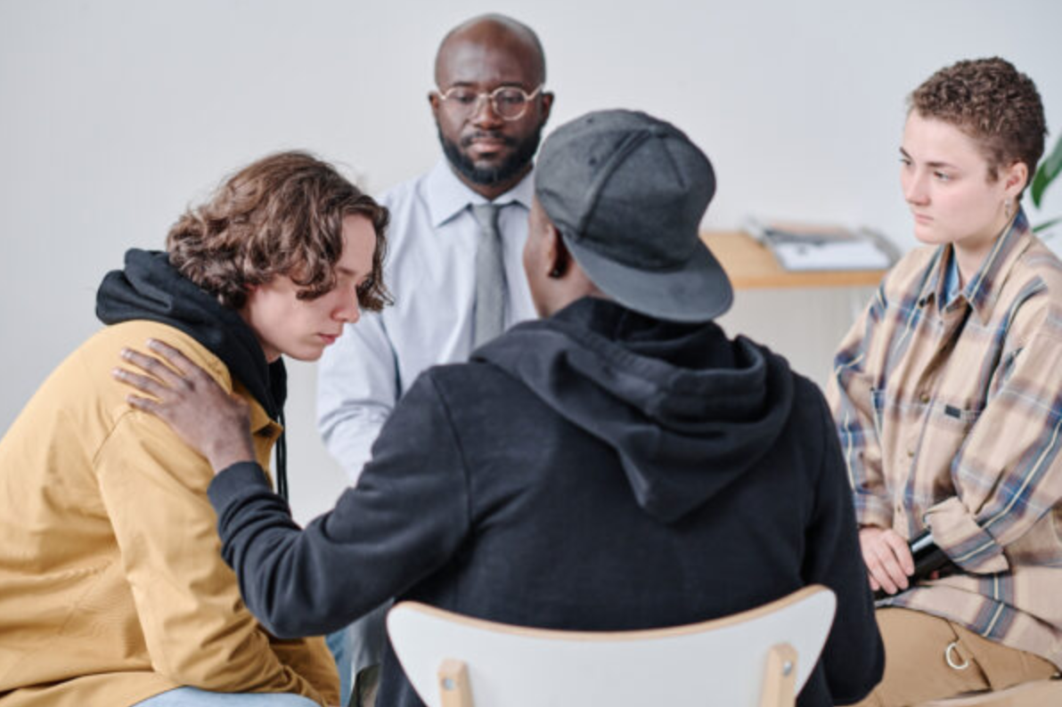 Teenage boy talking about problems to other people while they supporting him and giving advice during psychotherapy session